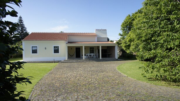Uma casa de dois andares com telhado em telhas, calçada pavimentada e varanda coberta com área de estar externa.