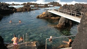 Uma nascente natural quente com água cristalina, arredores rochosos e uma ponte de madeira.