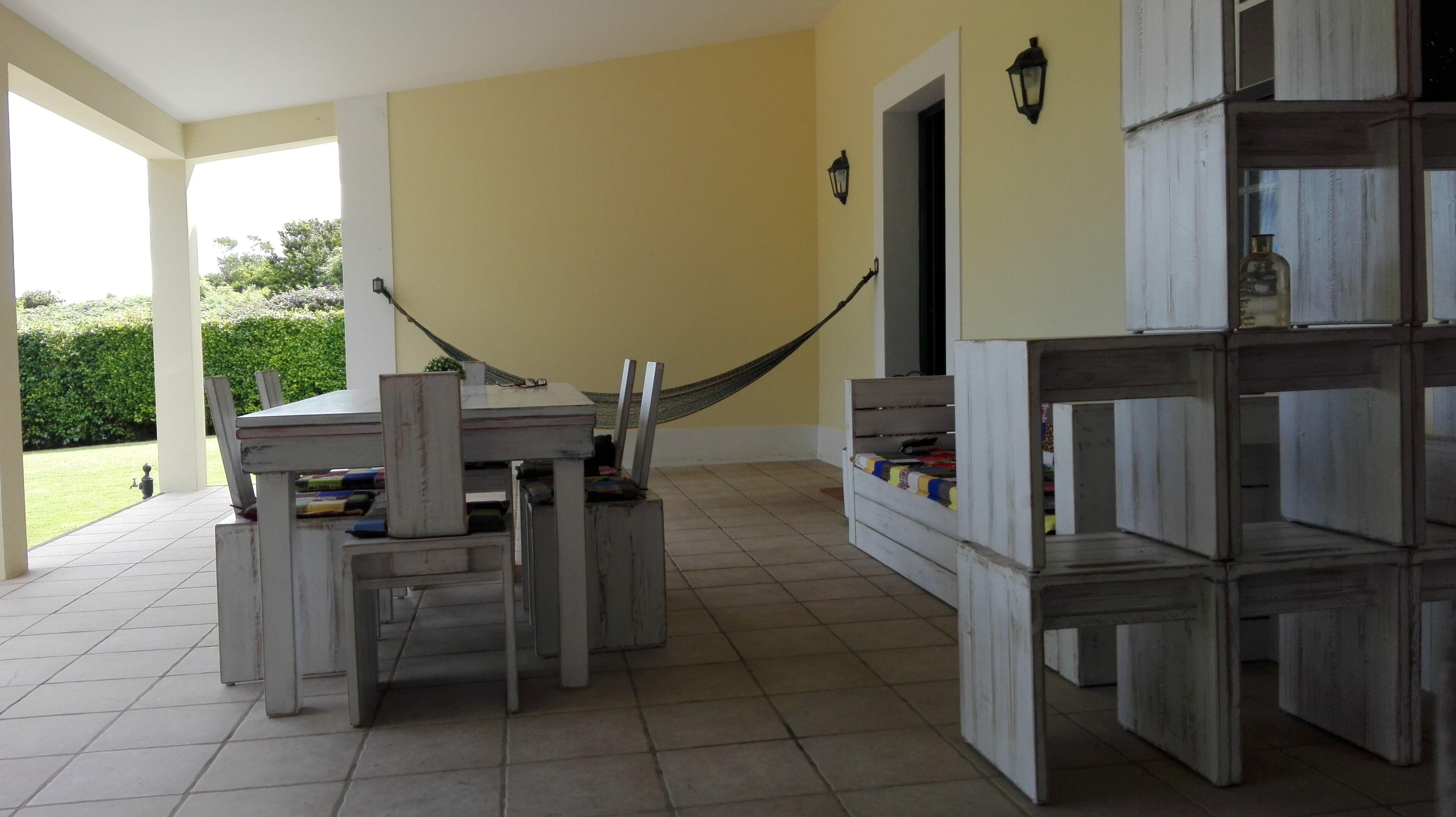 A covered patio with a dining table and chairs, a hammock, and a bookshelf.