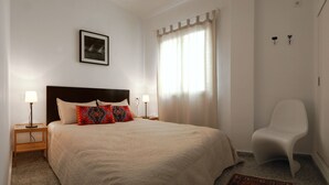 A neatly arranged bedroom with a bed, two bedside lamps, a chair, and a window with curtains. - Apart. 3, Casa Malaga with sea views & balcony (Málaga)