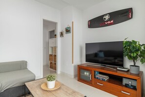 A modern living room with a grey sofa, a flat-screen TV, a wooden entertainment unit, and a potted plant.