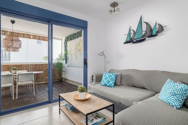 A modern living room with a grey sofa, a wooden coffee table, and a view through a glass door to an outdoor dining area.