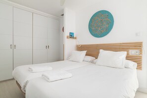 A bedroom with a bed, white bedding, a wooden headboard, a large wardrobe, and a decorative wall piece.