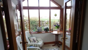 A cozy room with a view of a garden through large windows, a small round table, and two armchairs. - Pet friendly barn conversion with spectacular views, just for 2. (Crosby Garrett)