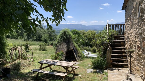 Un cadre extérieur rustique avec un banc en bois, une structure à toit de chaume et un escalier en pierre menant à un bâtiment.