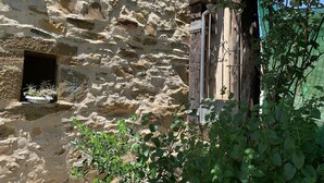 Un bâtiment en pierre avec une petite fenêtre et une porte surmontée d’un portail en métal.