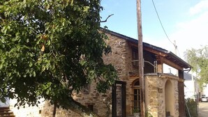 Un bâtiment en pierre avec un escalier en bois menant à une porte, le tout entouré d’arbres.