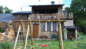 Une maison rustique en bois, avec des fondations en pierre, une balançoire en bois et une échelle.