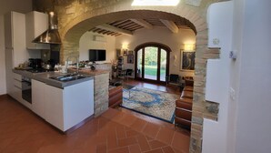 A spacious kitchen with an island, stone walls, and a large arched doorway leading to a living area with a view of the outdoors. - Stone house with private exclusive infinity pool in Chianti (San Filippo A Ponzano)