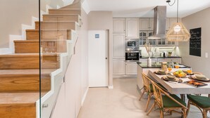 Een moderne keuken met houten trap, een eethoek met groene stoelen en een prikbord met een welkomstbericht.
