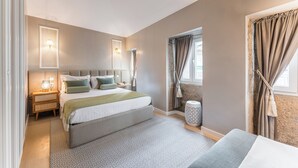 Een moderne slaapkamer met een groot bed, nachtkastjes, een lamp, een raam met gordijnen en een klein bijzettafeltje.