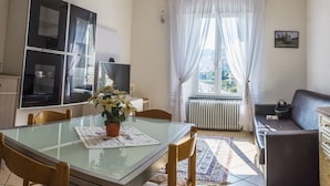 Un salón con una mesa de comedor de cristal, un sofá, un radiador y una ventana con cortinas.