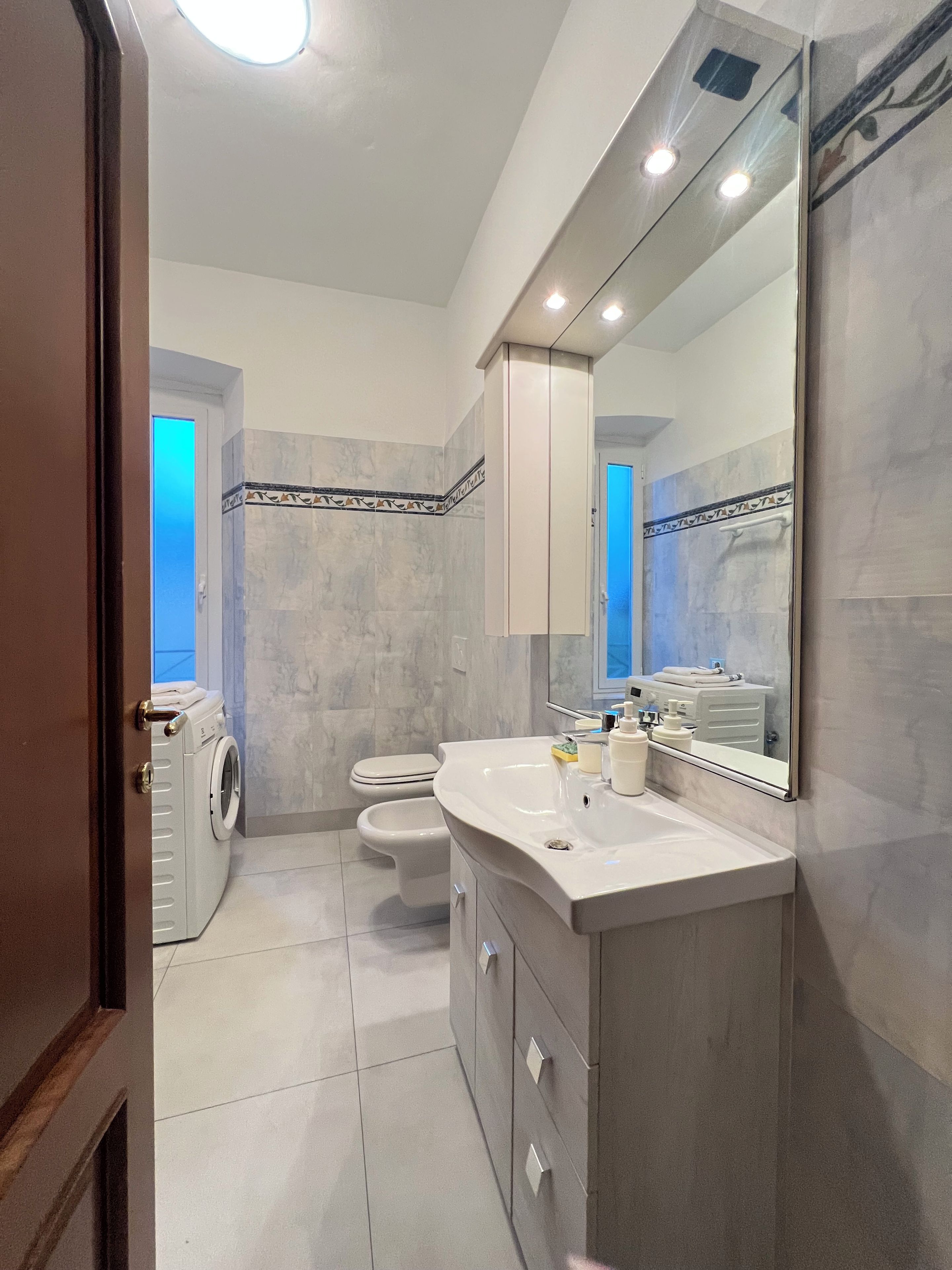 A bathroom with a washing machine, toilet, and a large mirror.