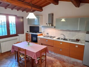 Uma cozinha com armários de madeira, fogão a gás, pia e mesa de jantar com cadeiras.
