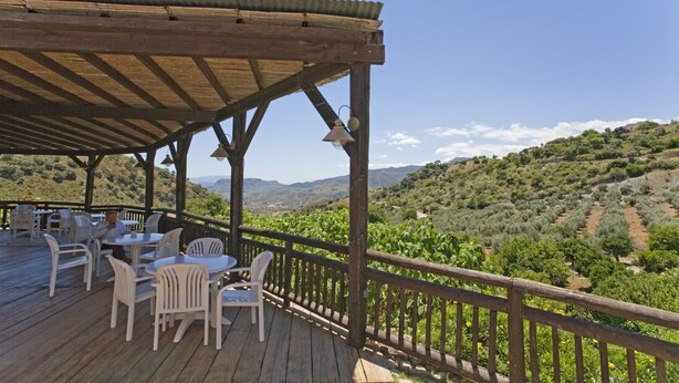 A wooden deck with white chairs and tables, overlooking a vineyard and hills. - El Mirador Rocabella Private Pool Apartment (Alora)