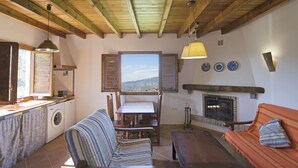 A cozy living area with a sofa, a table, and a fireplace. There is a window with a view of the outdoors. - El Mirador Rocabella Private Pool Apartment (Alora)