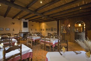 Uma sala de jantar com mesas e cadeiras de madeira, lareira e um bar.