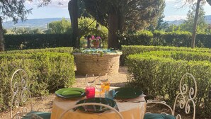 An outdoor dining setup with a table and chairs, surrounded by greenery and a view of the landscape. - Apartment in Farmhouse (Montepulciano)