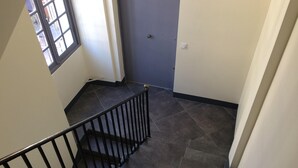 Una escalera con baldosas oscuras y barandilla negra, que conduce a una puerta con un interruptor de luz en la pared.