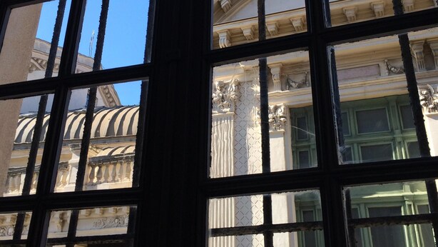 Vista a través de una ventana con un diseño de cuadrícula, mostrando arquitectura clásica con columnas y una cúpula.