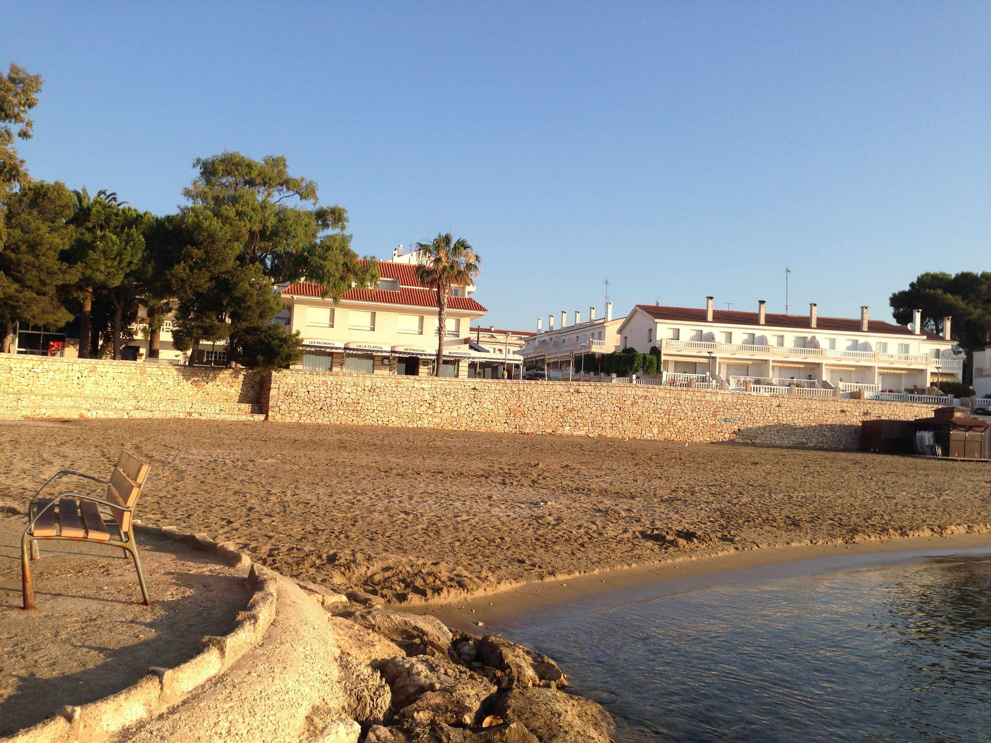 Un hôtel situé sur la côte, doté d’un mur en pierre, d’une plage et donnant sur une mer calme.
