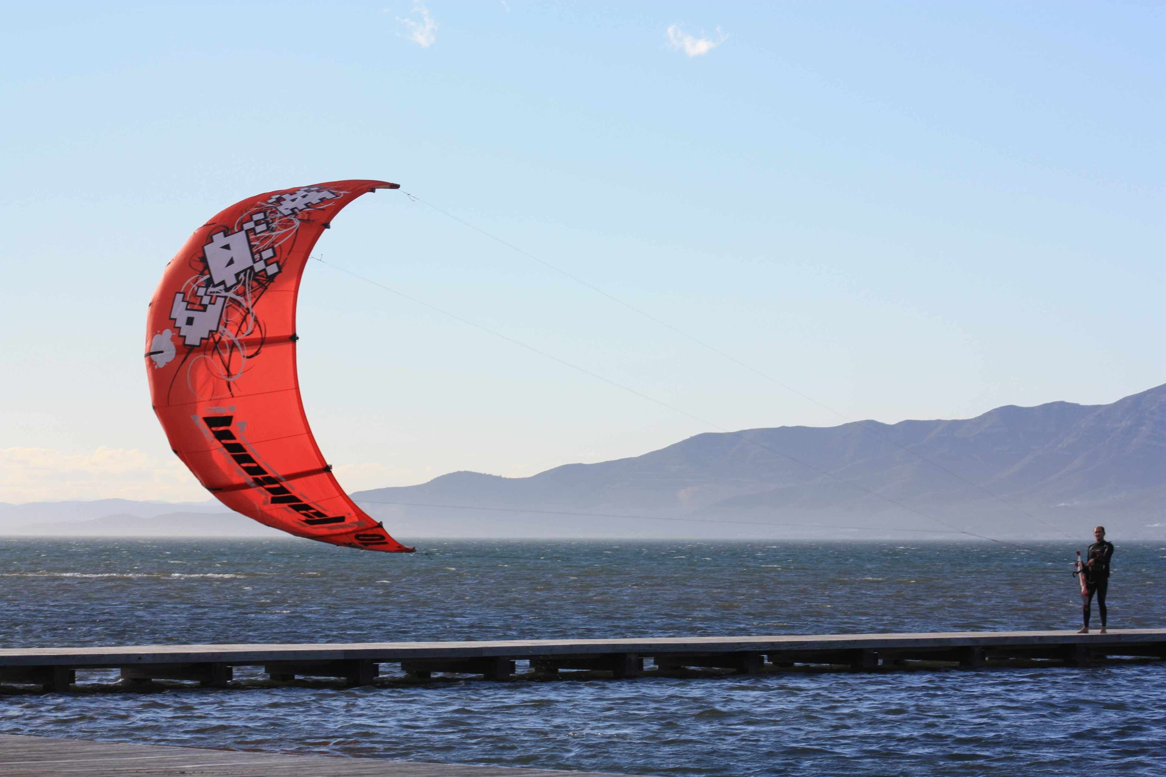 Una persona de pie en un muelle con una cometa roja.