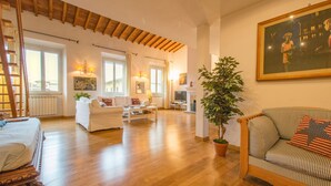 Uma sala de estar ampla com piso de madeira, um conjunto de sofás, uma mesa de centro e uma planta grande.