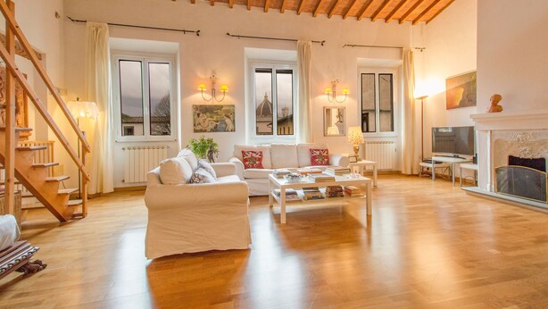 Uma sala de estar ampla com teto de madeira, sofás brancos, uma mesa de centro e uma lareira.