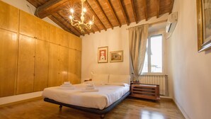 Quarto com teto de madeira, cama com roupa de cama branca, mesa de cabeceira e radiador.