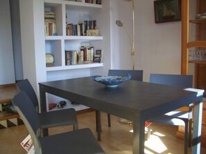 A dining area with a table, chairs, a bowl, and a bookshelf.