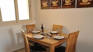 A dining table with four chairs, a bottle, and glasses. - 2 Bed Luxury Apartment Overlooking The Lush Gardens And Pools. With Spa And Gym For Guests (Mandria)