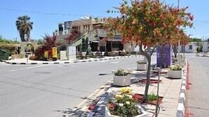 A street with a sidewalk lined with potted plants and flowers. There are buildings in the background, one with a balcony. - 2 Bed Luxury Apartment Overlooking The Lush Gardens And Pools. With Spa And Gym For Guests (Mandria)