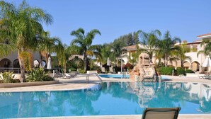 A pool area with lounge chairs, palm trees, and a stone fountain. - 2 Bed Luxury Apartment Overlooking The Lush Gardens And Pools. With Spa And Gym For Guests (Mandria)