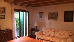 Un área de comedor con una mesa y sillas de madera, un sofá floral y una pequeña mesa con una lámpara.