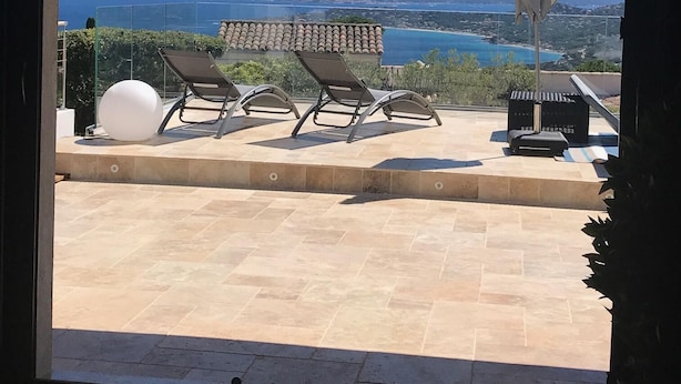 A balcony with two sun loungers, a white umbrella, and a stone floor.