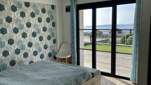 A bedroom with a bed, a chair, a view of the outdoors, and a patterned wall.