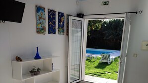 Ein Schlafzimmer mit einem Bett, einem Fernseher, einem Regal mit Dekoration und Blick auf einen Swimmingpool.