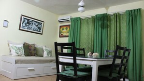 A room with a bed, a dining table with chairs, a ceiling fan, and green curtains.