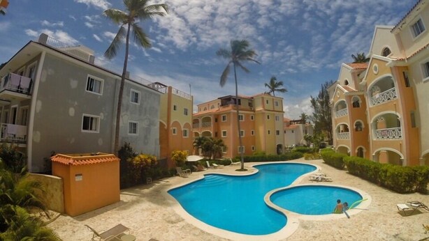 A resort with a central swimming pool, palm trees, and multi-story buildings with balconies.