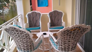 A balcony with two white wicker chairs with blue cushions, a small round table, and a blue curtain in the background.