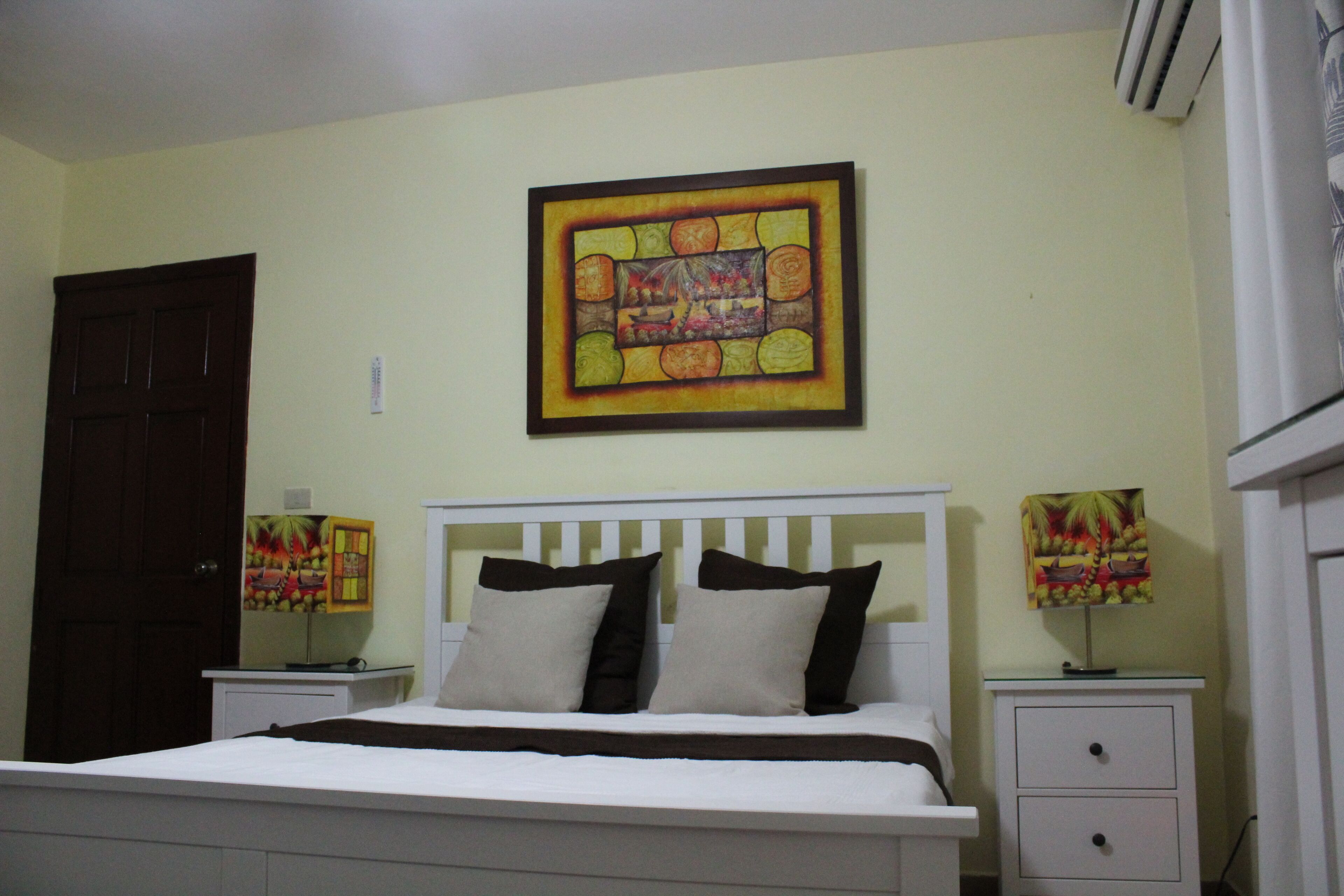 A bedroom with a bed, two bedside tables, a nightstand, a door, and a wall-mounted picture.