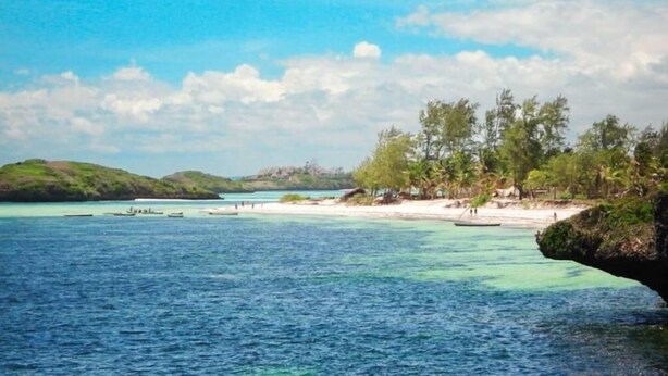 Eine Küstenlandschaft mit klarem, blauem Wasser, einem Sandstrand und einer kleinen Insel in der Ferne.