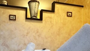 Una cama bien hecha con toallas blancas enrolladas, un aplique de pared y cuadros enmarcados.