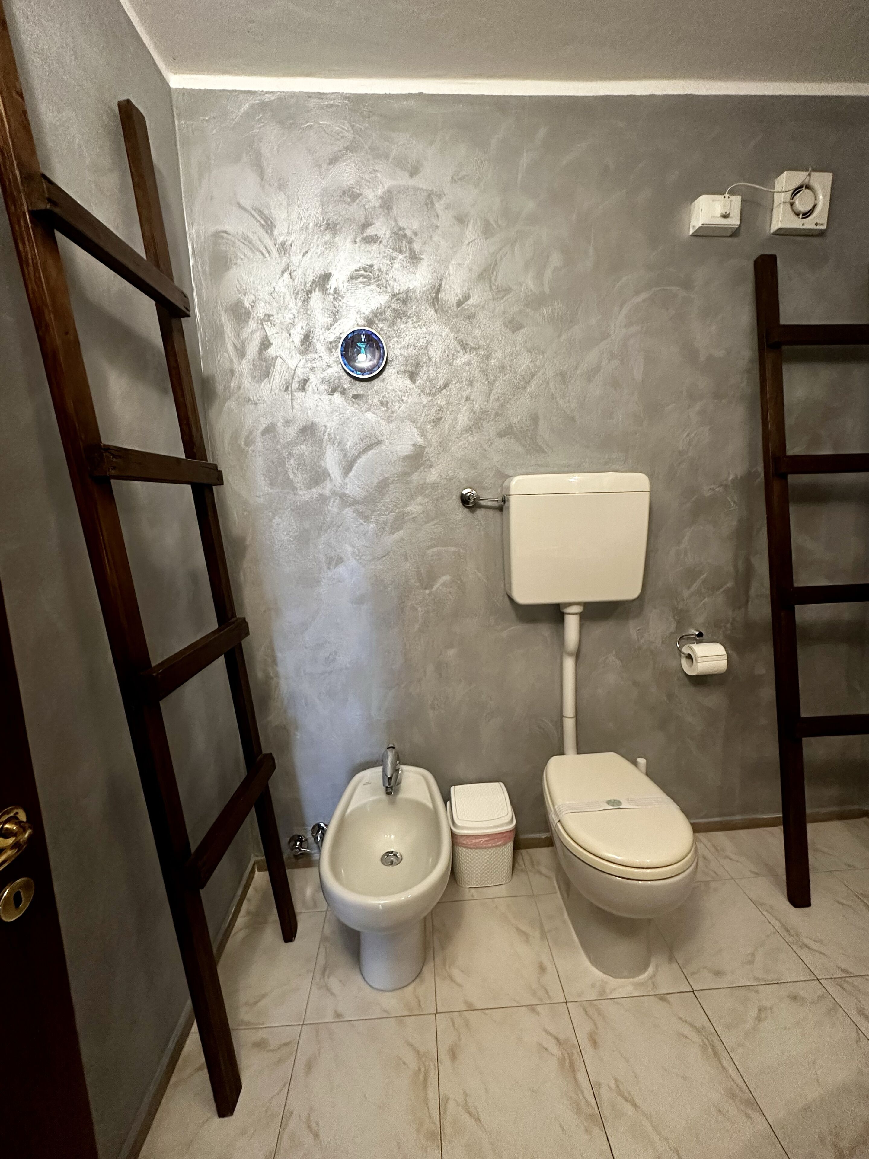 Kylpyhuoneessa on wc, bidee ja pesuallas. Seinää vasten on nojattu tikkaat ja seinällä on wc-paperiteline.