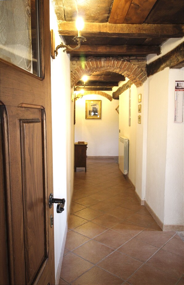 A narrow hallway with wooden doors and a tiled floor, leading to a room with a radiator and a framed picture on the wall.