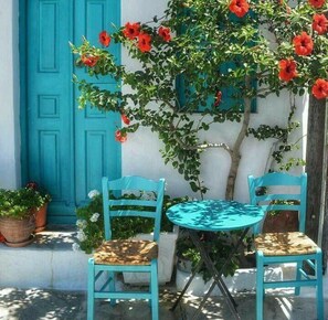 A blue door, a small round table with two chairs, and a tree with red flowers.