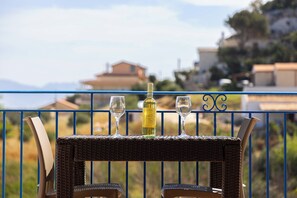 A balcony with wicker furniture, two glasses, and a bottle of wine.