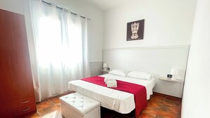 A hotel room with two beds, a red and white bedspread, a white bench, a nightstand with a lamp, and a painting on the wall. - APARTMENT IN VILLA 200 METERS FROM THE SEA WI FI CAR RENTAL UC (castellammare del golfo)