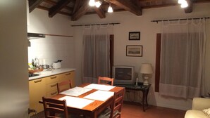 Un comedor acogedor con una mesa y sillas de madera, un televisor sobre una mesita y una cocina al fondo.