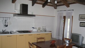 Una cocina con estufa, lavamanos y gabinetes blancos. Hay una mesa de comedor con sillas y un televisor sobre un mueble.
